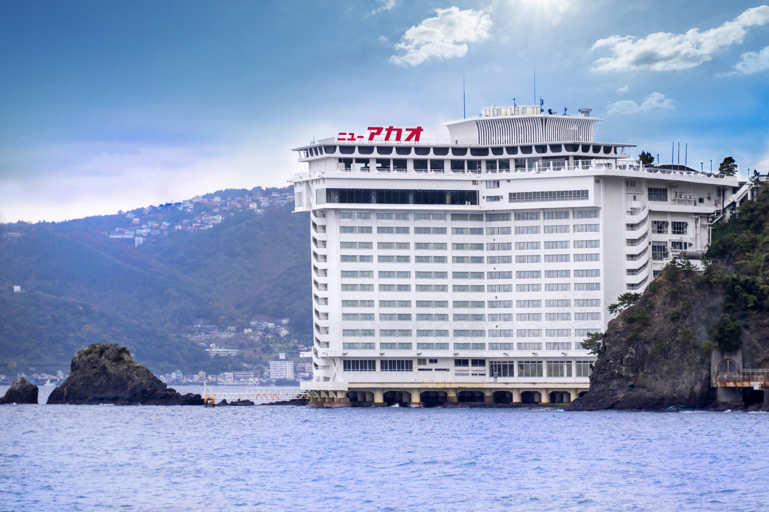 歴史を刻んだ岩が複雑に重なる、美しく迫力のある景観、エメラルド色の押し波に洗われる名勝「錦ヶ浦」に聳え立つ【ホテルニューアカオ】